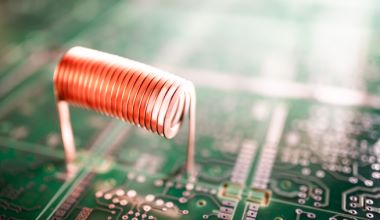 Closeup twisted copper wire stands on a green microcircuit. Computer hardware concept. Factory for the production of oscillatory circuit and high-frequency equipment