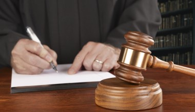 A gavel and block rests on a judge's desk while the magistrate takes notes in his law library preparing to oversee a case.